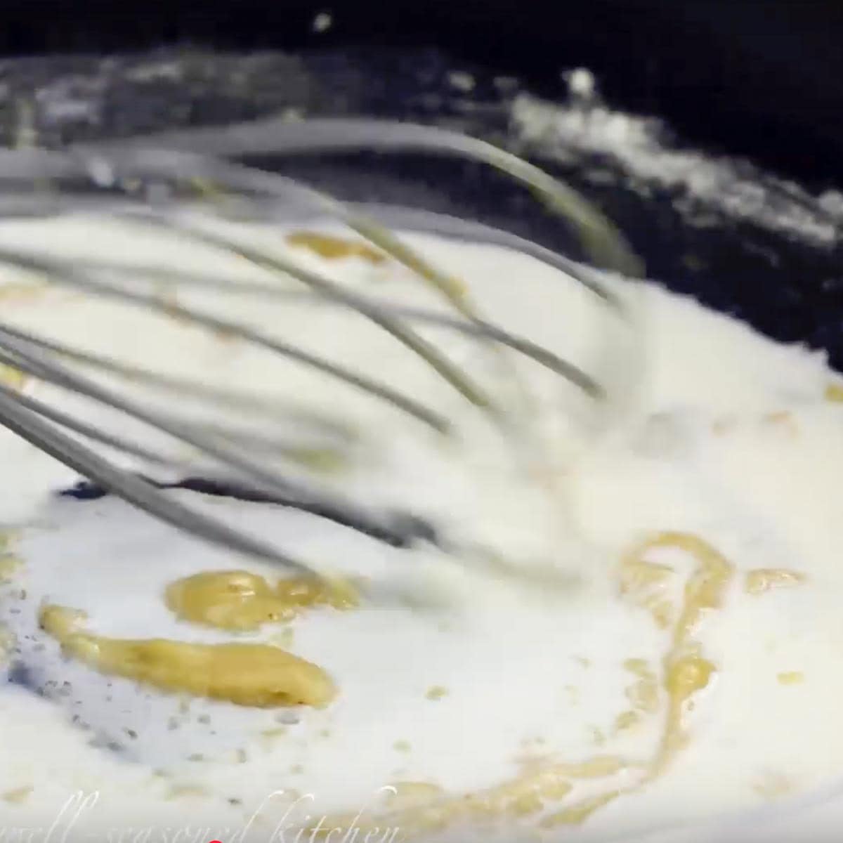 Milk added to the skillet with a whisk stirring it into the roux.