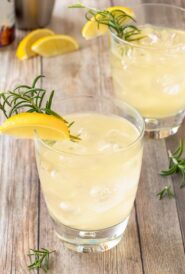two clear cocktail glasses holding Lemon Ginger Mocktails, garnished with lemon wedge and rosemary sprig