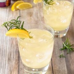 two clear cocktail glasses holding Lemon Ginger Mocktails, garnished with lemon wedge and rosemary sprig