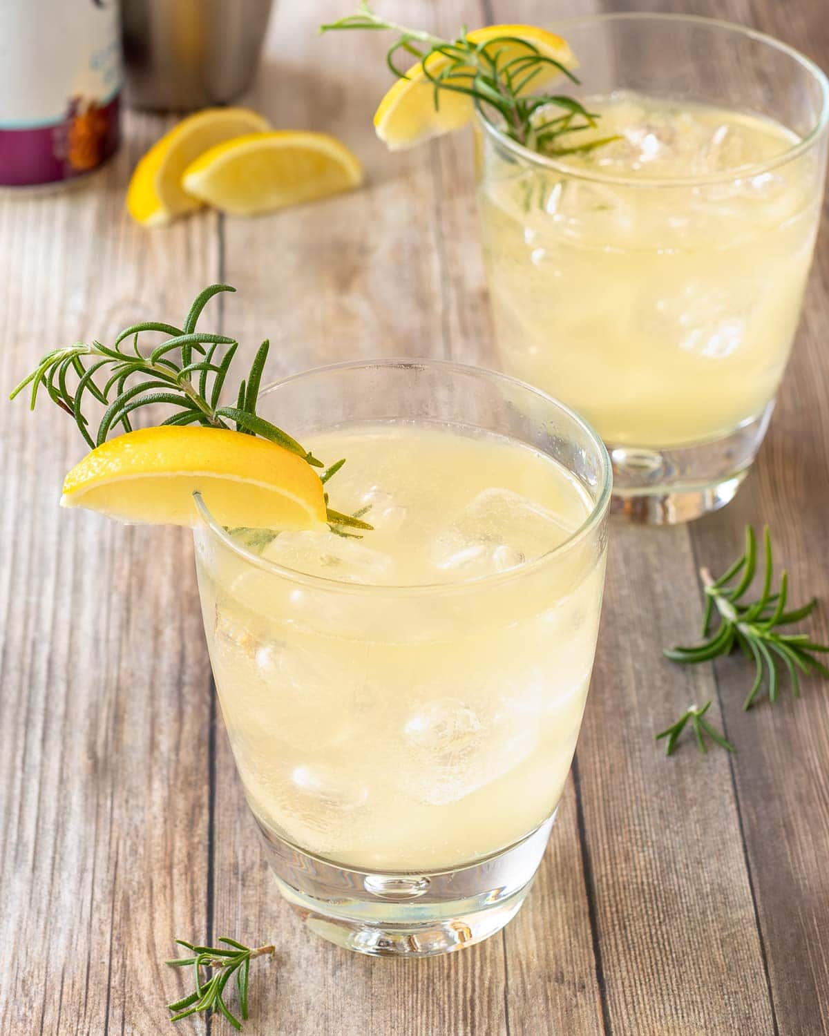 two clear cocktail glasses holding Lemon Ginger Mocktails, garnished with lemon wedge and rosemary sprig