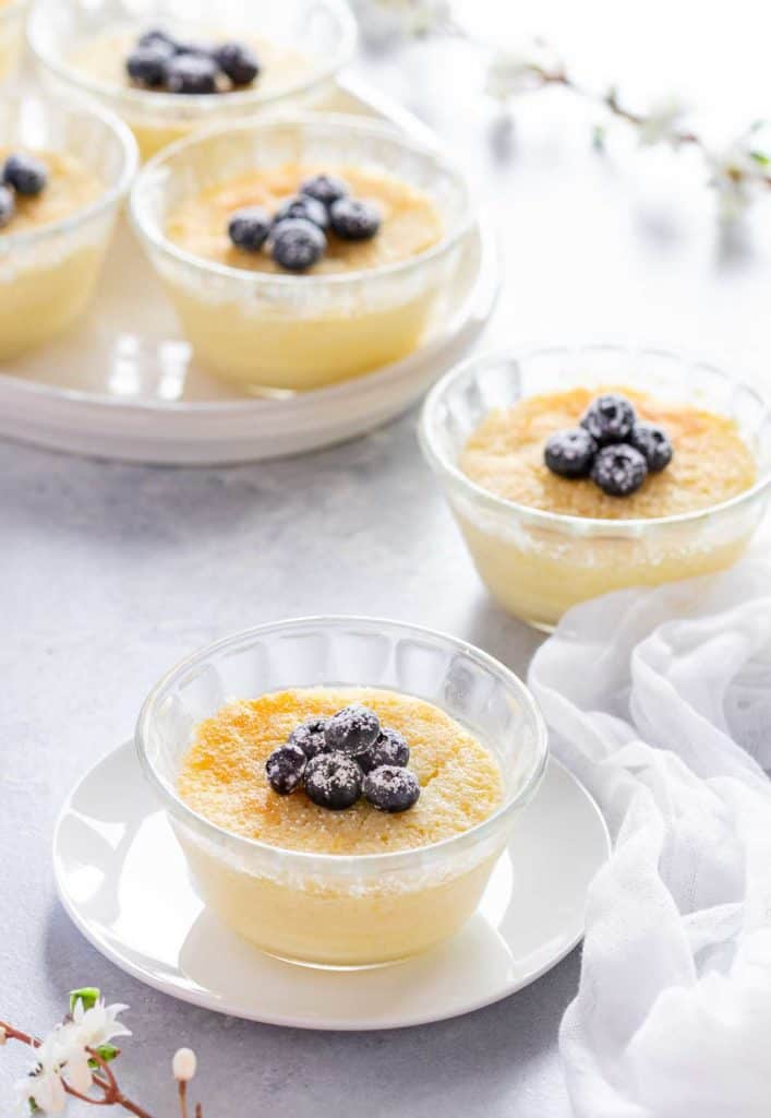 Small glass dishes holding baked Lemon Pudding Cups, showing garnish of blueberries