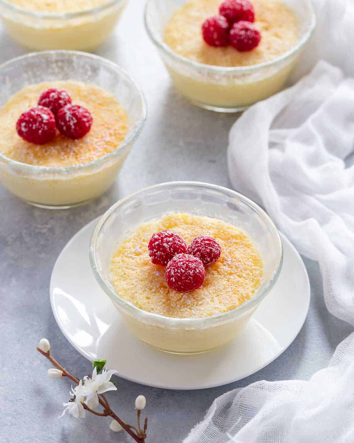 Small glass dishes holding Lemon Pudding Cups, showing alternate garnish of raspberries.