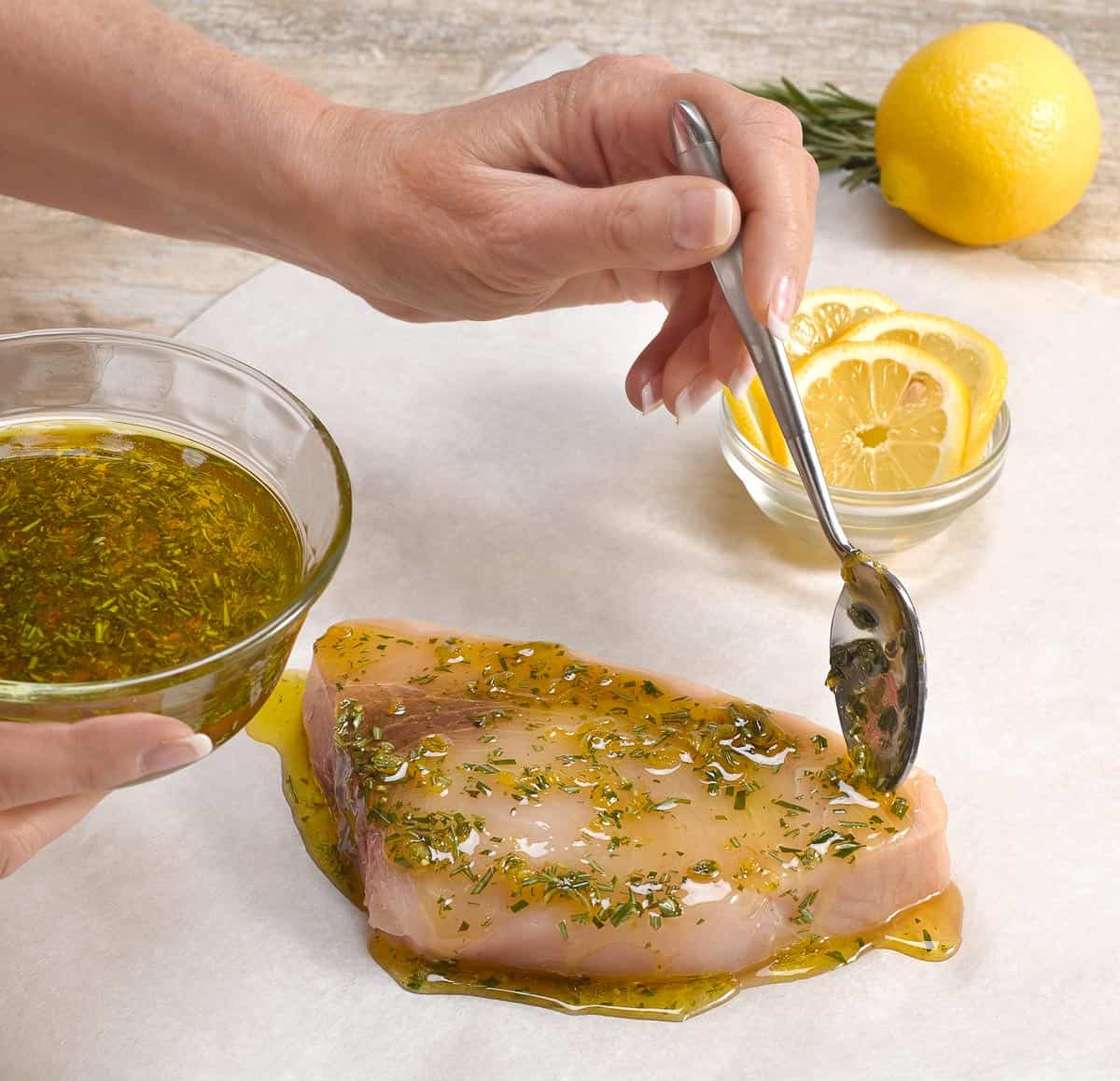 showing swordfish filet on papillote paper, hand adding marinade