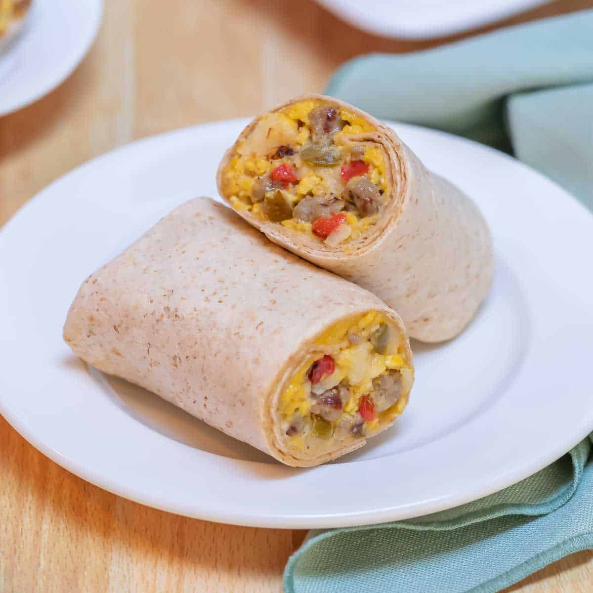white plate holding one Make Ahead Breakfast Burrito, cut in half to show moist stuffing.