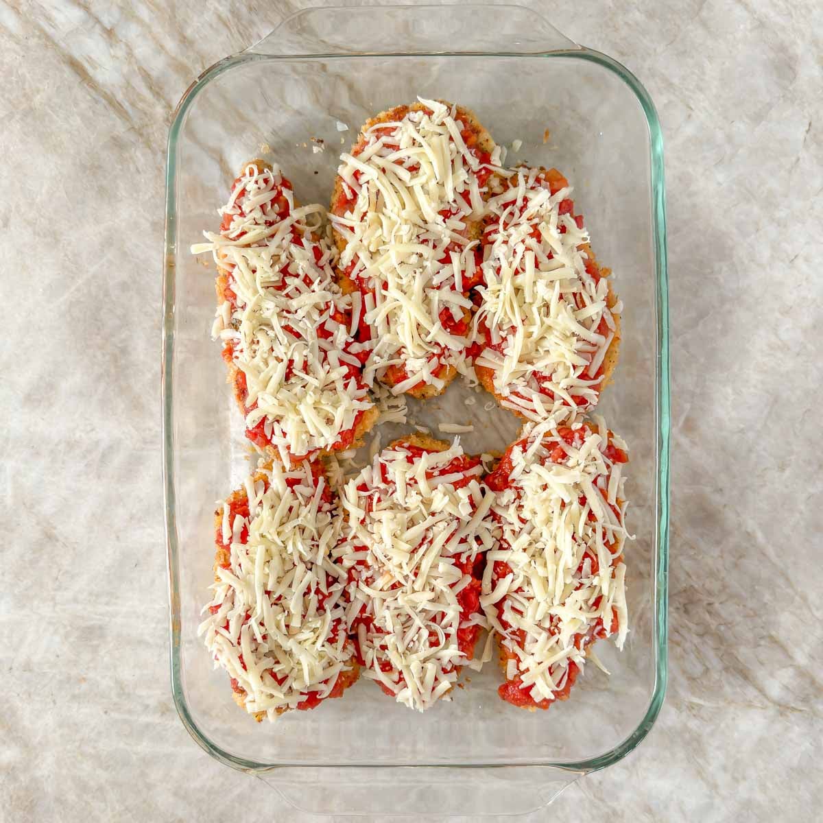 6 breaded and pan seared chicken breasts topped with shredded Mozzarella, ready for baking..