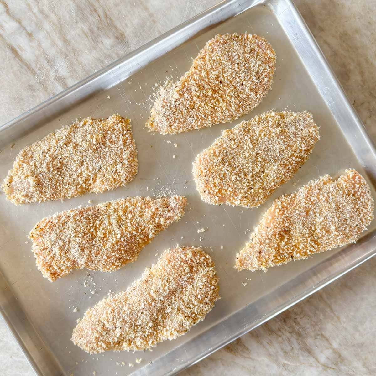 Breaded chicken cutlets on a sheet pan ready to refrigerate for make-ahead chicken parmesan.