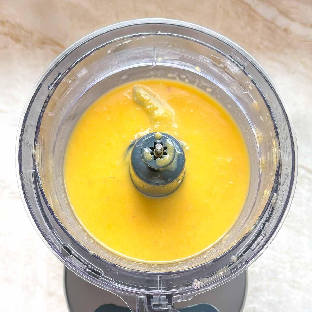 Puréed mango vinaigrette ingredients inside a food processor, showing smooth texture of the dressing.