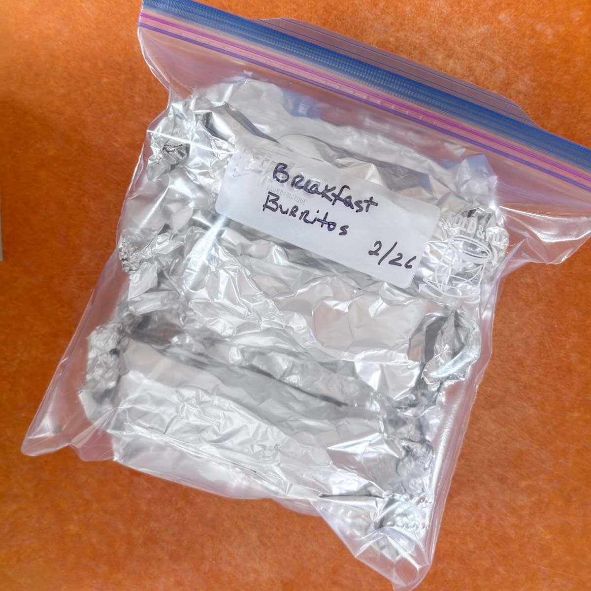 Foil-wrapped breakfast burritos inside a freezer-safe ziptop baggie, labeled with name and date.