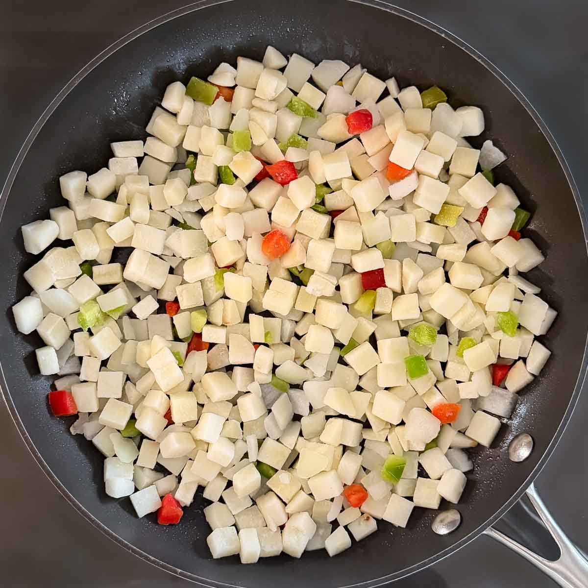 Potatoes O'Brien arranged in a single layer in a large skillet, not cooked yet.
