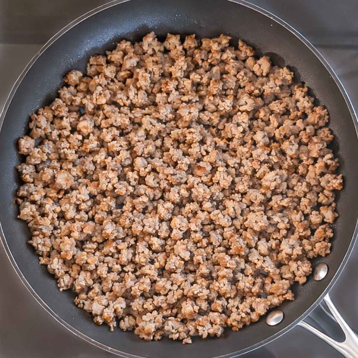 Turkey sausage crumbles browning in a skillet.