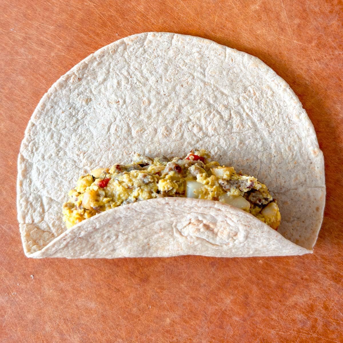 Flour tortilla on cutting board with the bottom edge folder halfway over the filling.