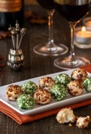 white platter holding 10 cheese truffles, 5 Cheddar-Pecan and 5 Fontina-Prosciutto cheese balls 2 wine glasses and a bottle are partially shown in the background