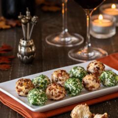 white platter holding 10 cheese truffles, 5 Cheddar-Pecan and 5 Fontina-Prosciutto cheese balls 2 wine glasses and a bottle are partially shown in the background