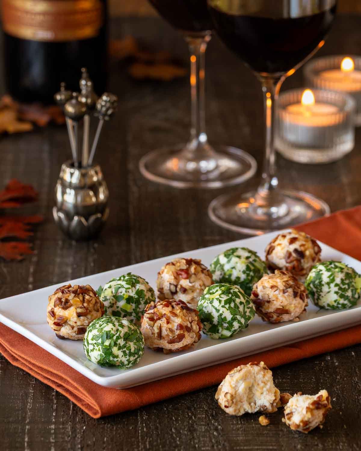 white platter holding 10 cheese truffles, 5 Cheddar-Pecan and 5 Fontina-Prosciutto cheese balls 2 wine glasses and a bottle are partially shown in the background