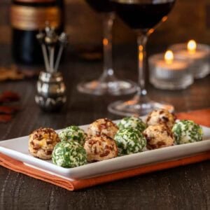 white platter holding 10 cheese truffles, 5 Cheddar-Pecan and 5 Fontina-Prosciutto cheese balls 2 wine glasses and a bottle are partially shown in the background