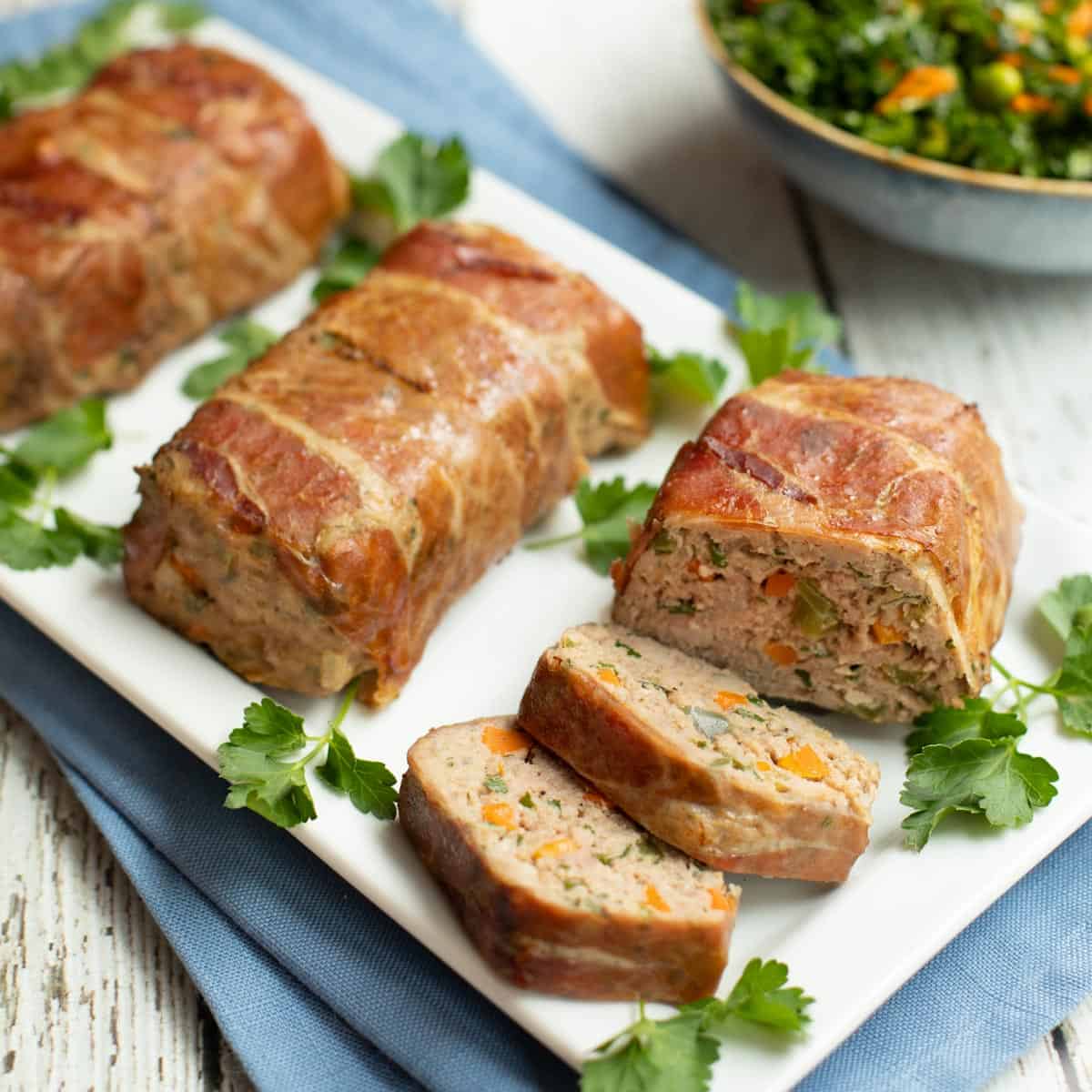 Mini Meatloaves Wrapped In Prosciutto, one sliced, on a white platter