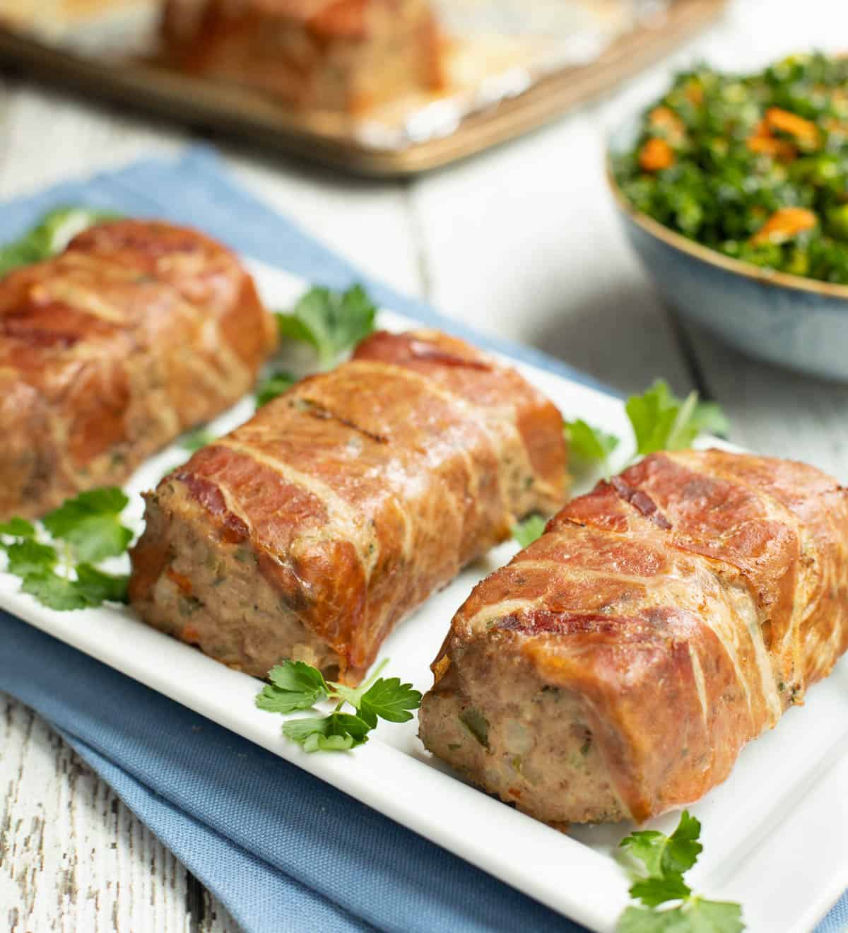 Mini Meatloaves Wrapped in Prosciutto on a white platter with a tossed kale sald