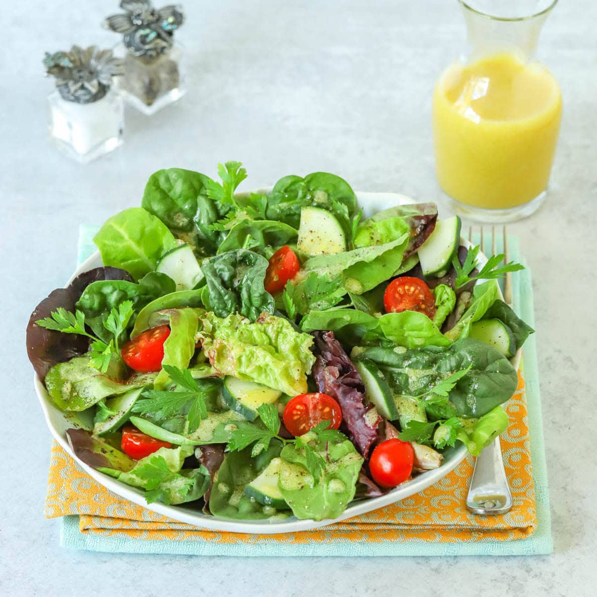 Plate holding a mixed green salad, with a carafe of Dijon Vinaigrette and small salt and pepper shakers.