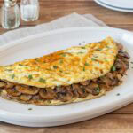 Light mushroom omelet filled with sautéed cremini mushrooms and onions on a white plate.
