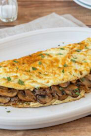 Light mushroom omelet filled with sautéed cremini mushrooms and onions on a white plate.
