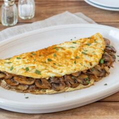 Light mushroom omelet filled with sautéed cremini mushrooms and onions on a white plate.
