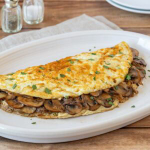 Light mushroom omelet filled with sautéed cremini mushrooms and onions on a white plate.
