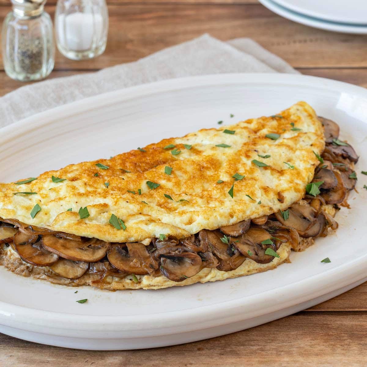 Light mushroom omelet filled with sautéed cremini mushrooms and onions on a white plate.