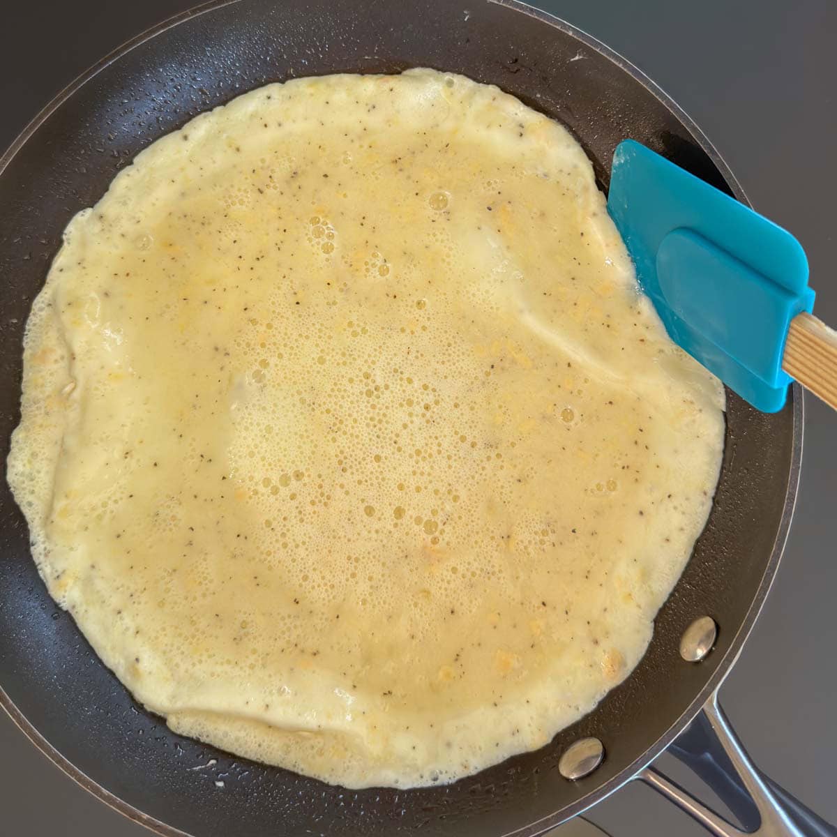 Rubber spatula lifting omelet edge to allow uncooked egg to flow underneath when pan is tilted.