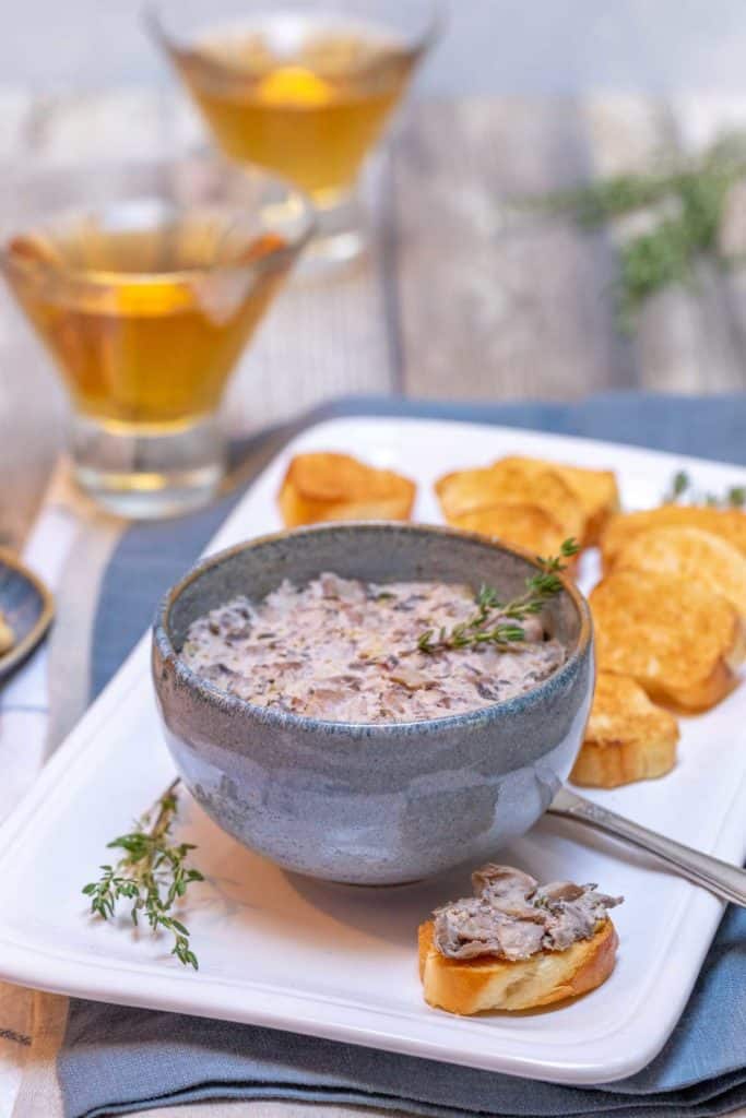 Blue bowl filled with Mushroom Pate; scoop of pate on a slice of bread in front to show single serving