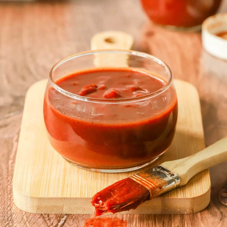 glass bowl holding Oklahoma Barbecue Sauce with a basting brush in front, with sauce on it.