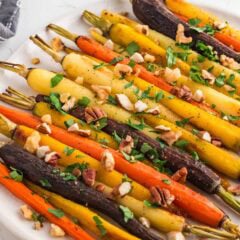 Roasted carrots in oven on a platter garnished with fresh herbs.