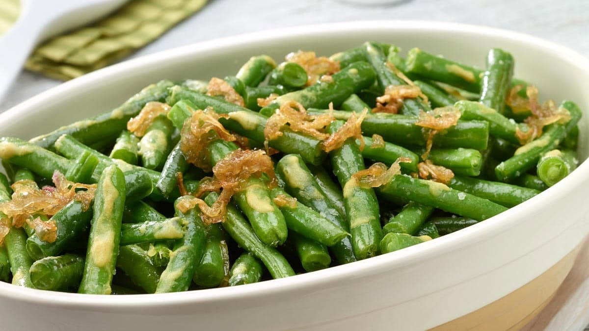 Horizontal close up photo of roasted green beans with dressing and crispy shallots