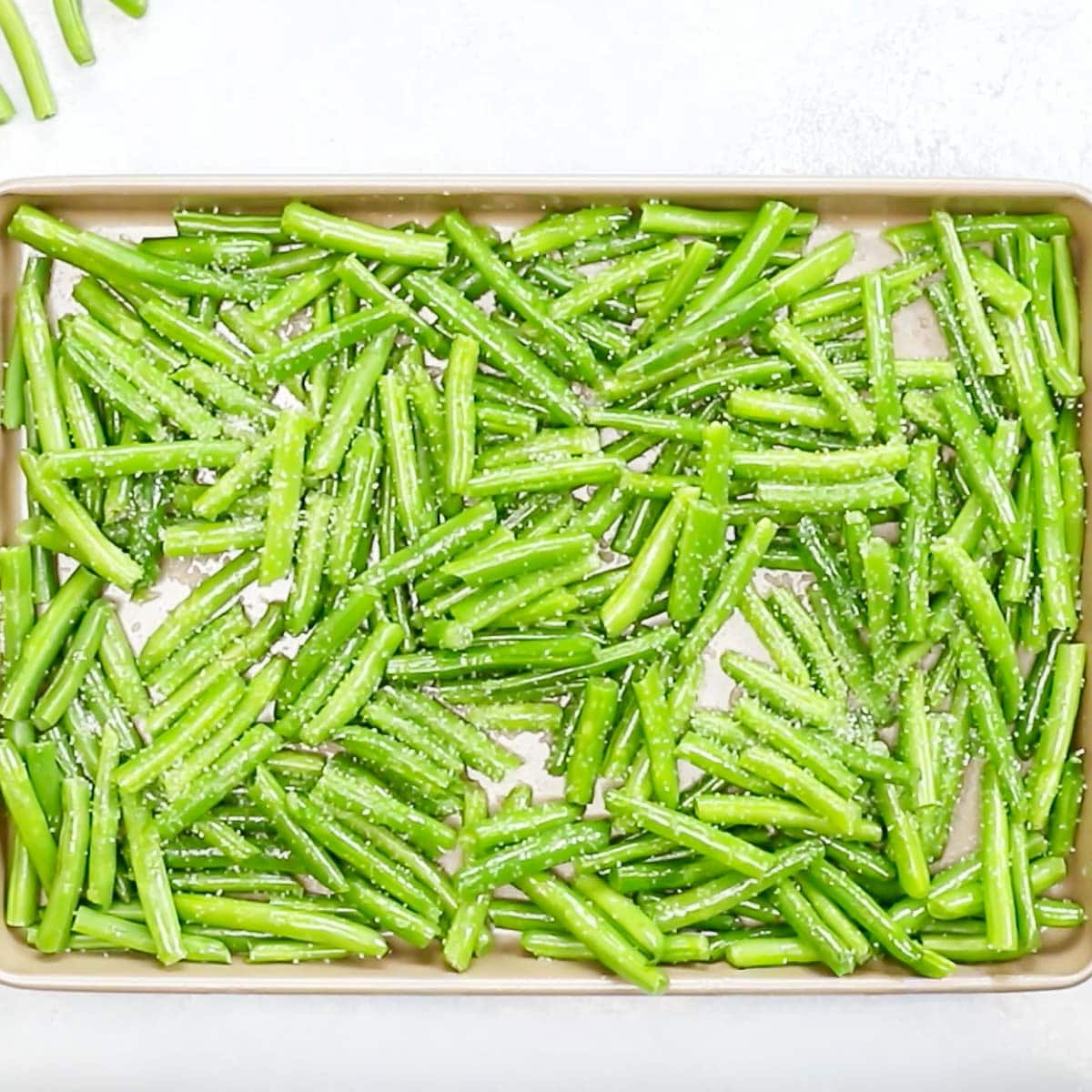 overhead view of green beans on a large rimmed cookie sheet, tossed with olive oil and salt