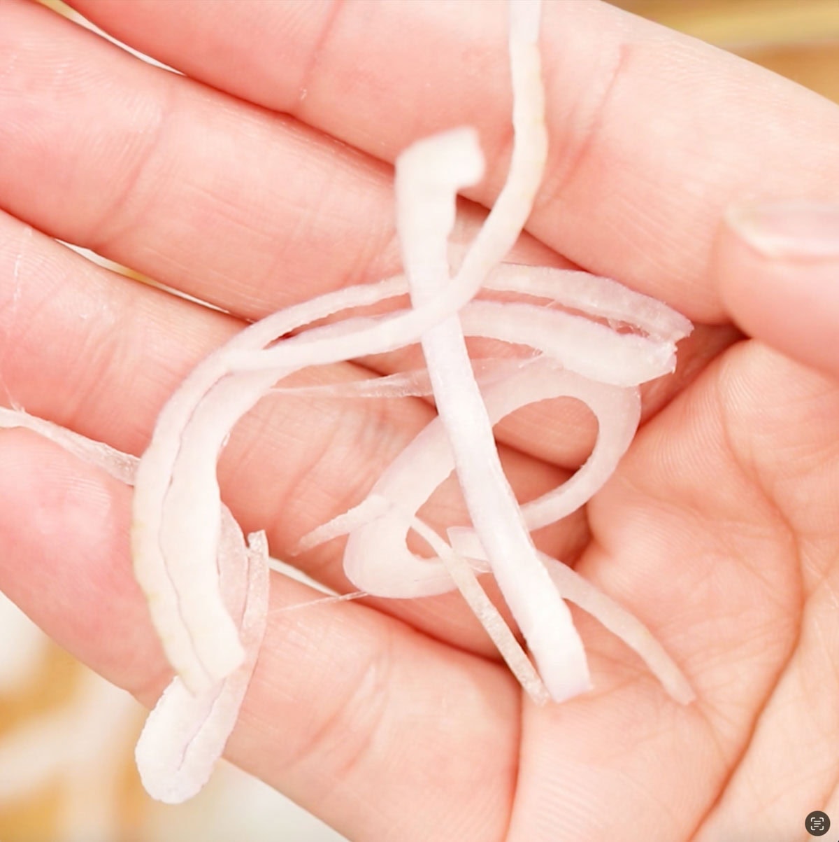 A hand holding up some slices of shallot.
