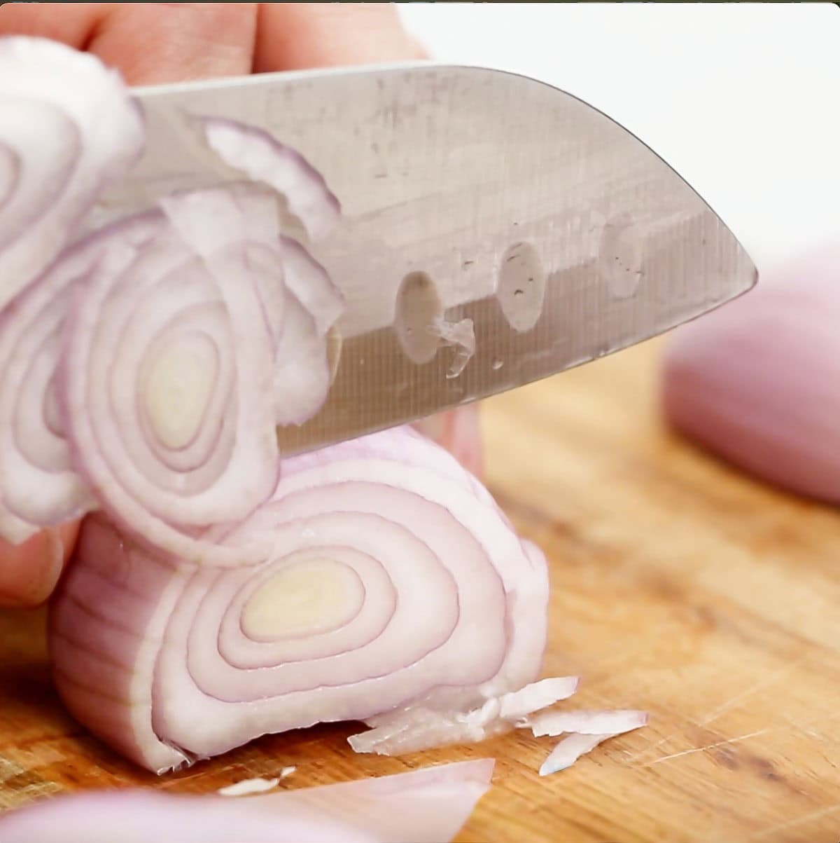 A knife slicing a shallot on a cutting board.