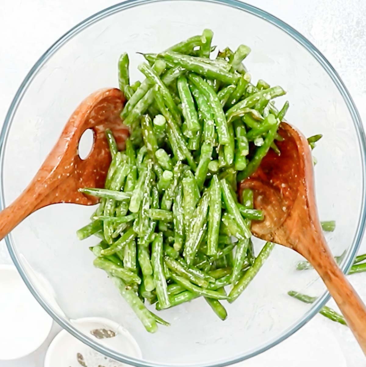 bowl with roasted green beans and lemon dijon dressing, with tossers in the bowl