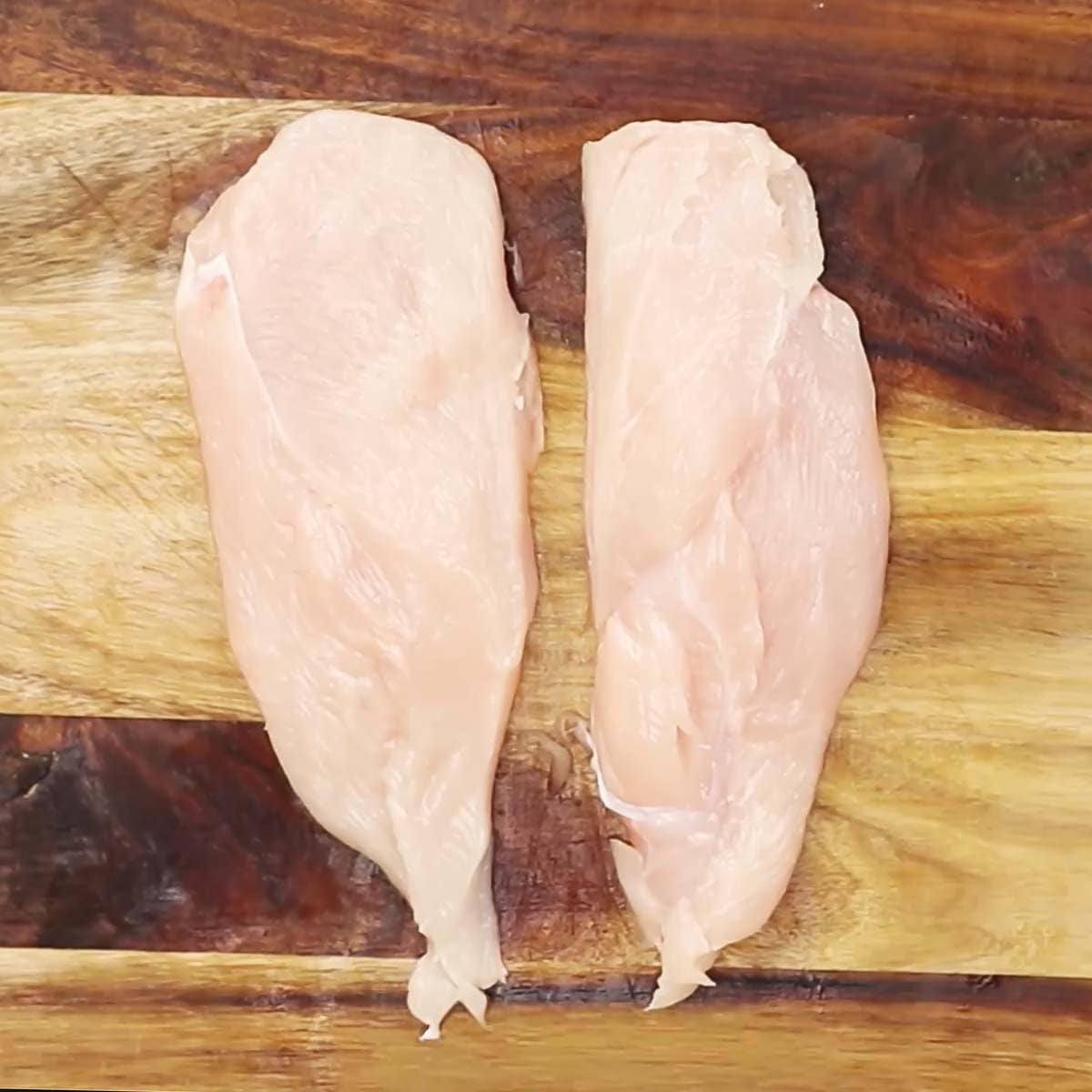 Chicken breast cut into half on a cutting board. 