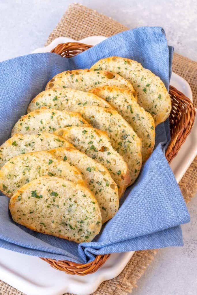 small basket lined with a blue napkin and filled with slices of Parsley Parmesan Crostini Bread