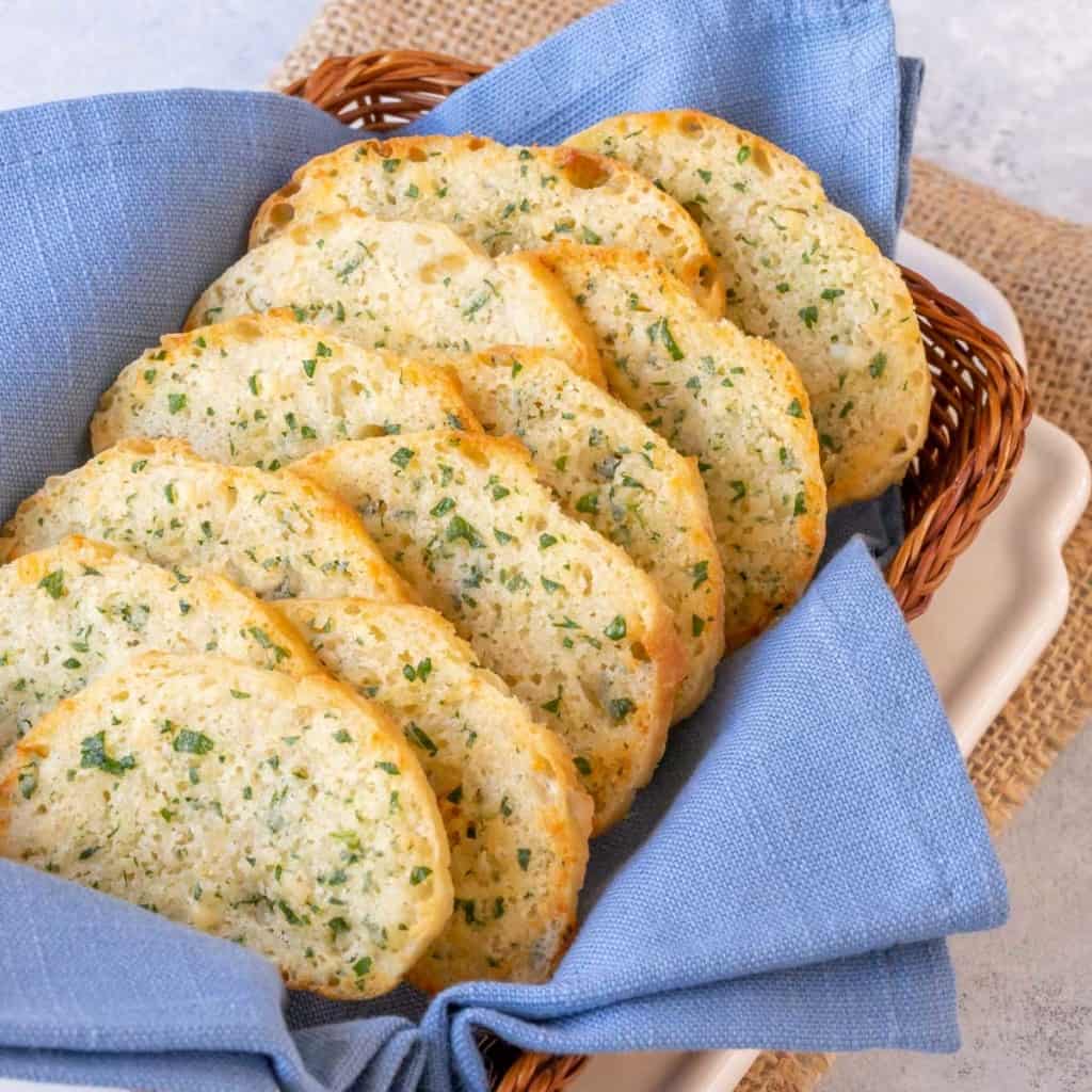 small basket lined with a blue napkin and filled with slices of Parsley Parmesan Crostini Bread
