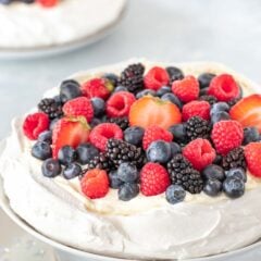 One Pavlova on a cake stand, with a second one and a bowl of berries in the background