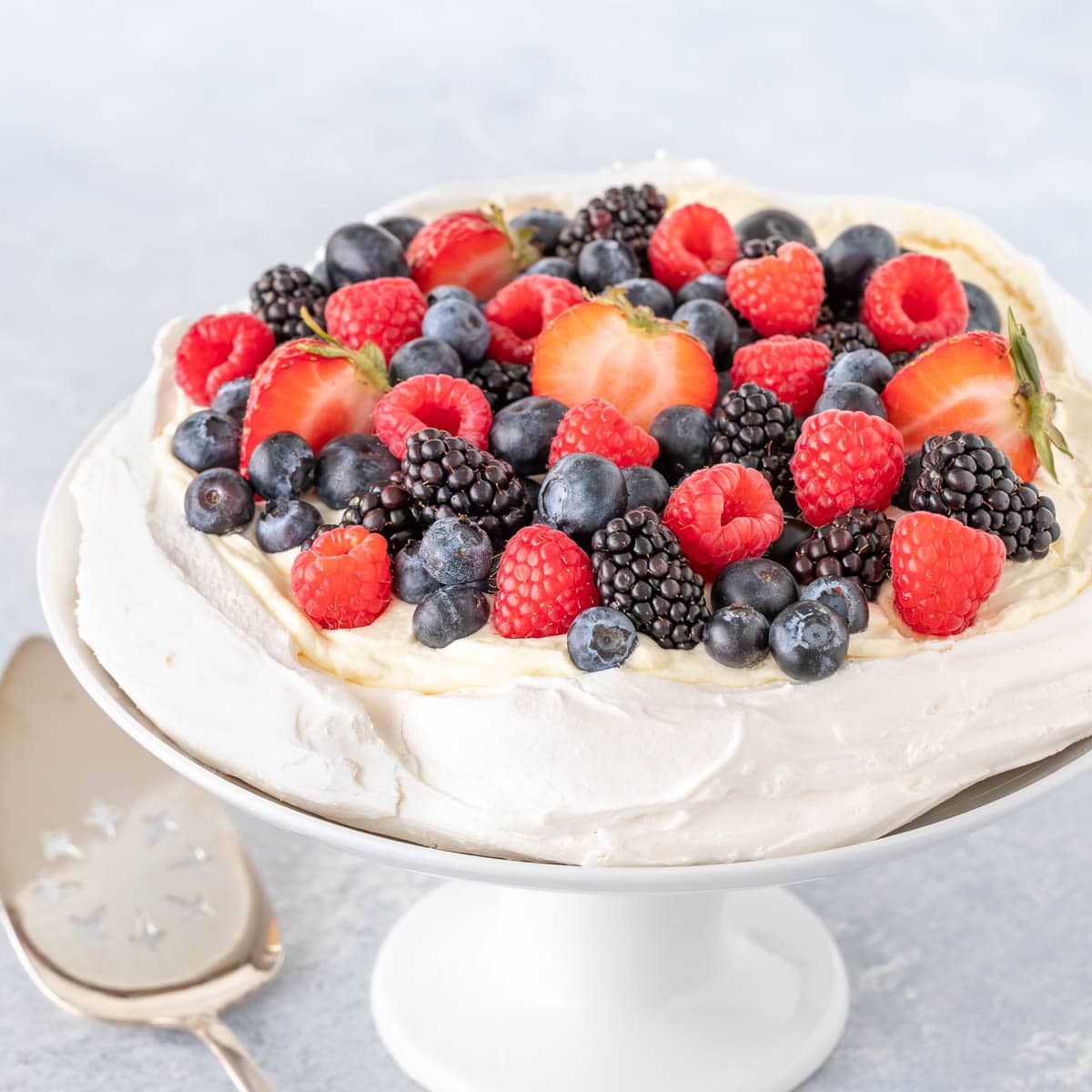 Close up of a Pavlova on a cake stand with fresh berries on top
