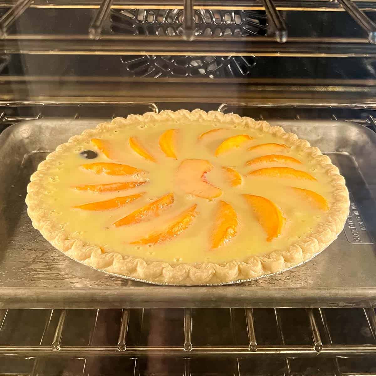 pie in oven baking, showing peaches floating in custard filing
