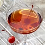 Coupe glass holding a single serving of Robert's Manhattan cocktail, garnished with a cherry.