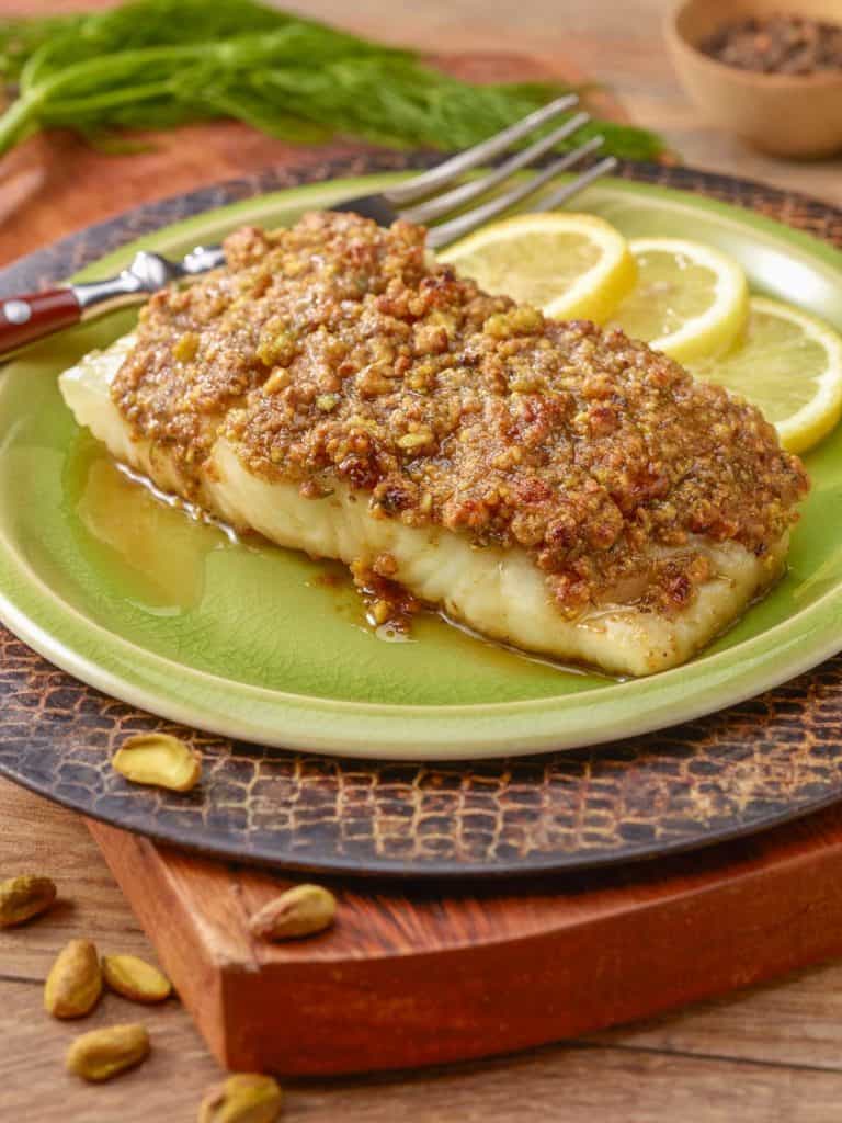 A single serving of Pistachio Crusted Fish, sitting on a light green plate that's on a cutting board. 