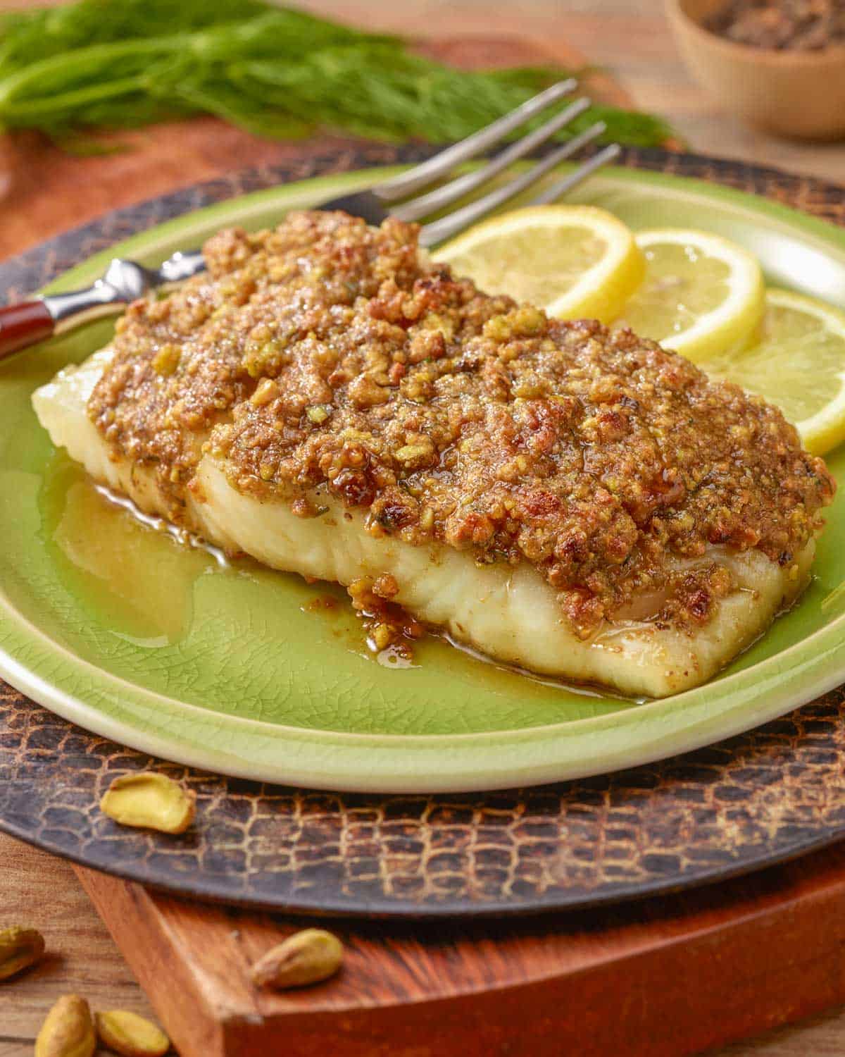 A single serving of Pistachio Crusted Fish, sitting on a light green plate that's on a cutting board.