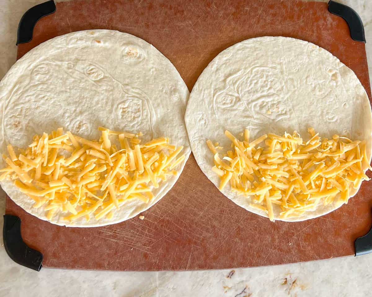 Overhead shot of two flour tortillas, open, with grated cheese on half of each.