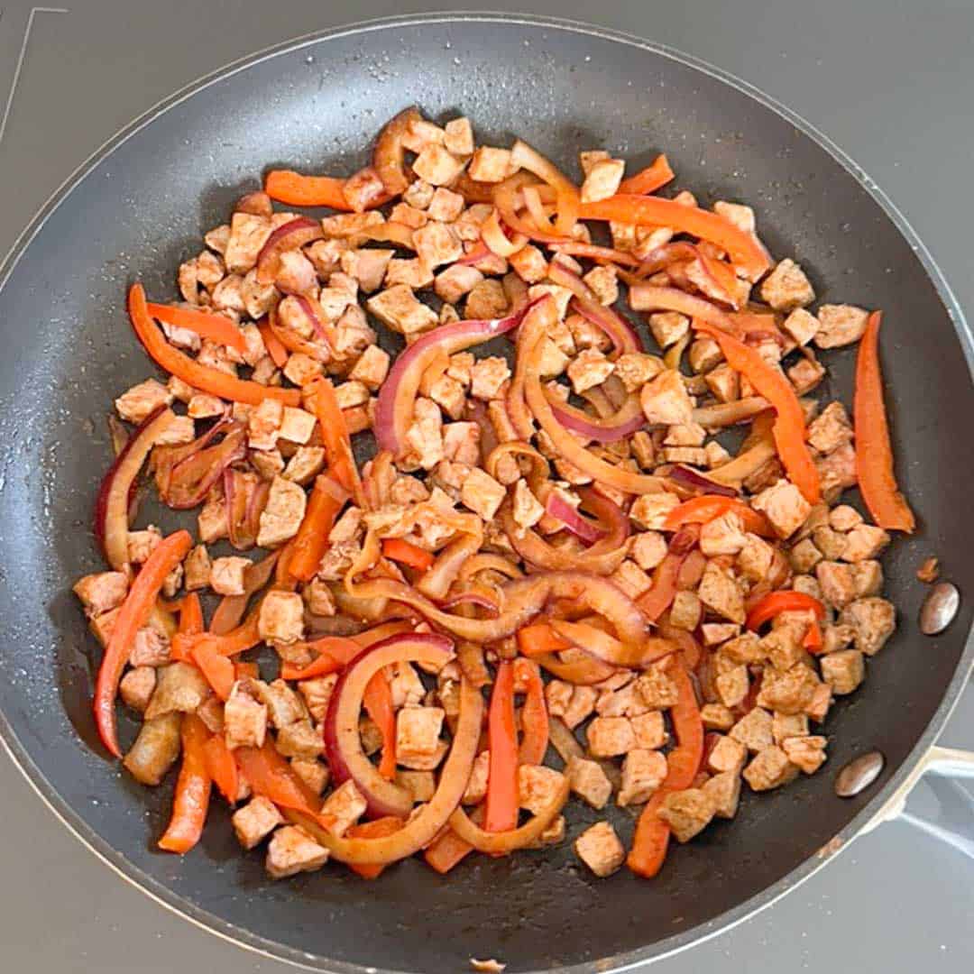 overhead shot of cooking onions, peppers, pork and sausage in a skillet