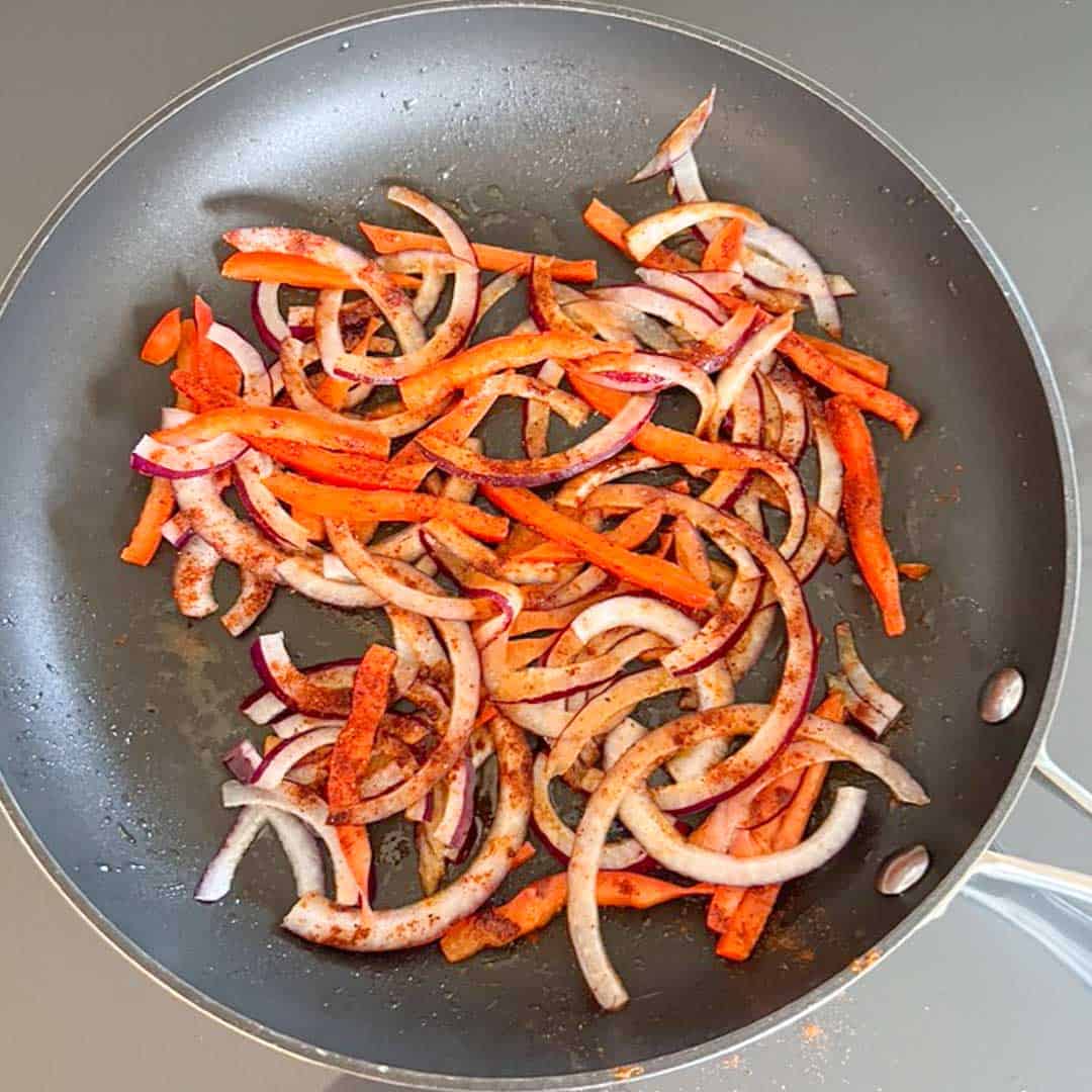 overhead shot of cooking onions and peppers in a skillet.