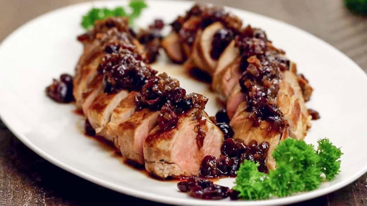 Juicy stuffed pork tenderloin with cranberry and Dijon sauce on white plate.