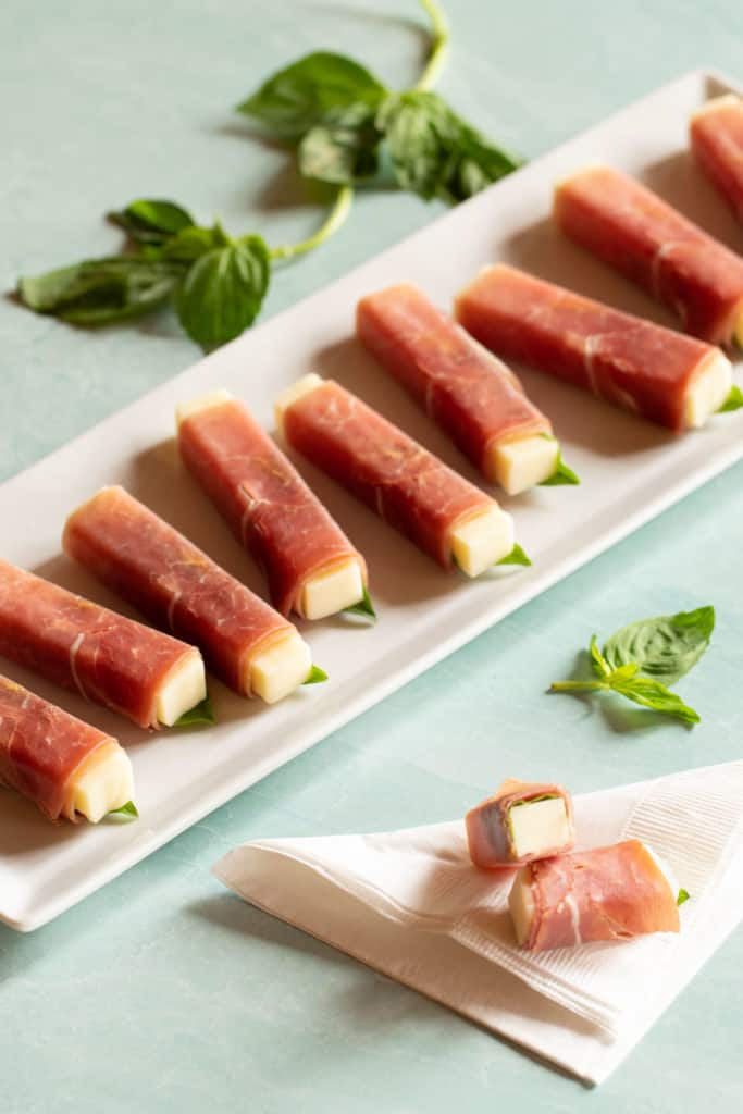 White rectangular platter filled with Prosciutto-Wrapped Smoked Mozzarella Sticks